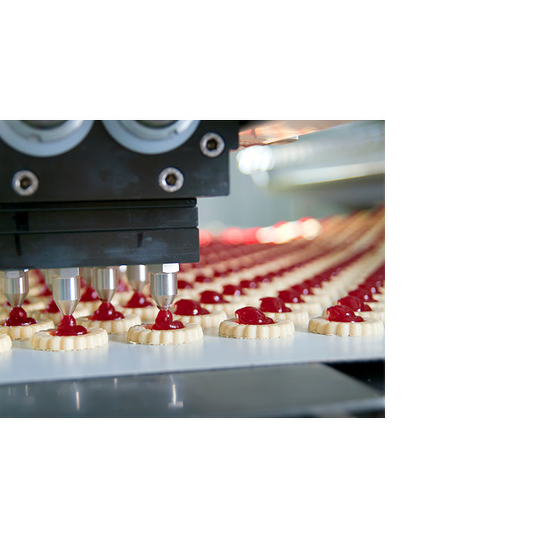 Machine automatisée appliquant de la confiture rouge aux biscuits dans une ligne de production alimentaire.